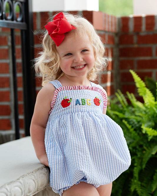 little girl wearing a seersucker bubble with "ABC" embroidered on the front