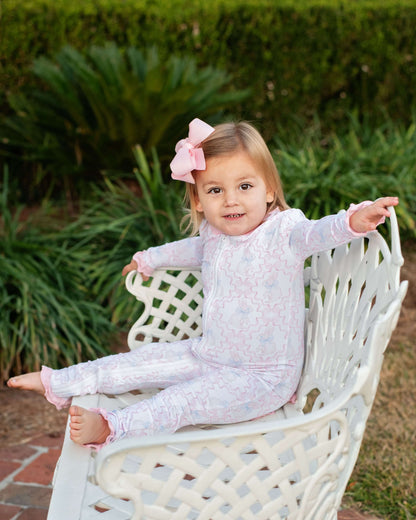 Young girl in a light purple outfit sitting on a white chair outdoors.