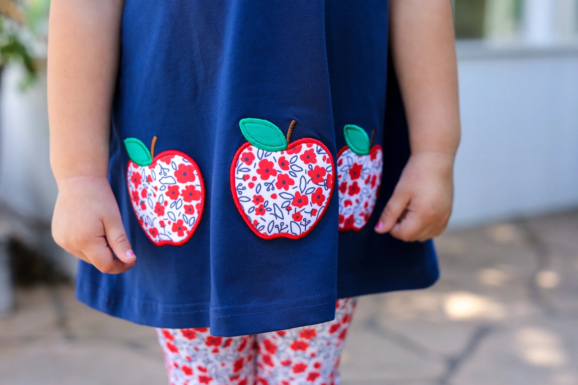 Navy blue dress with floral apple appliqués worn by a child.