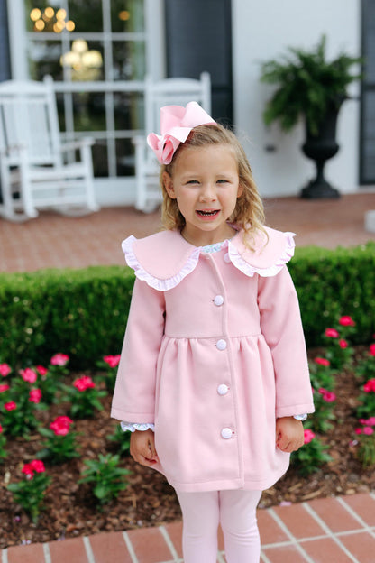 girl in a pink outfit with a bow, standing outdoors in front of a house.