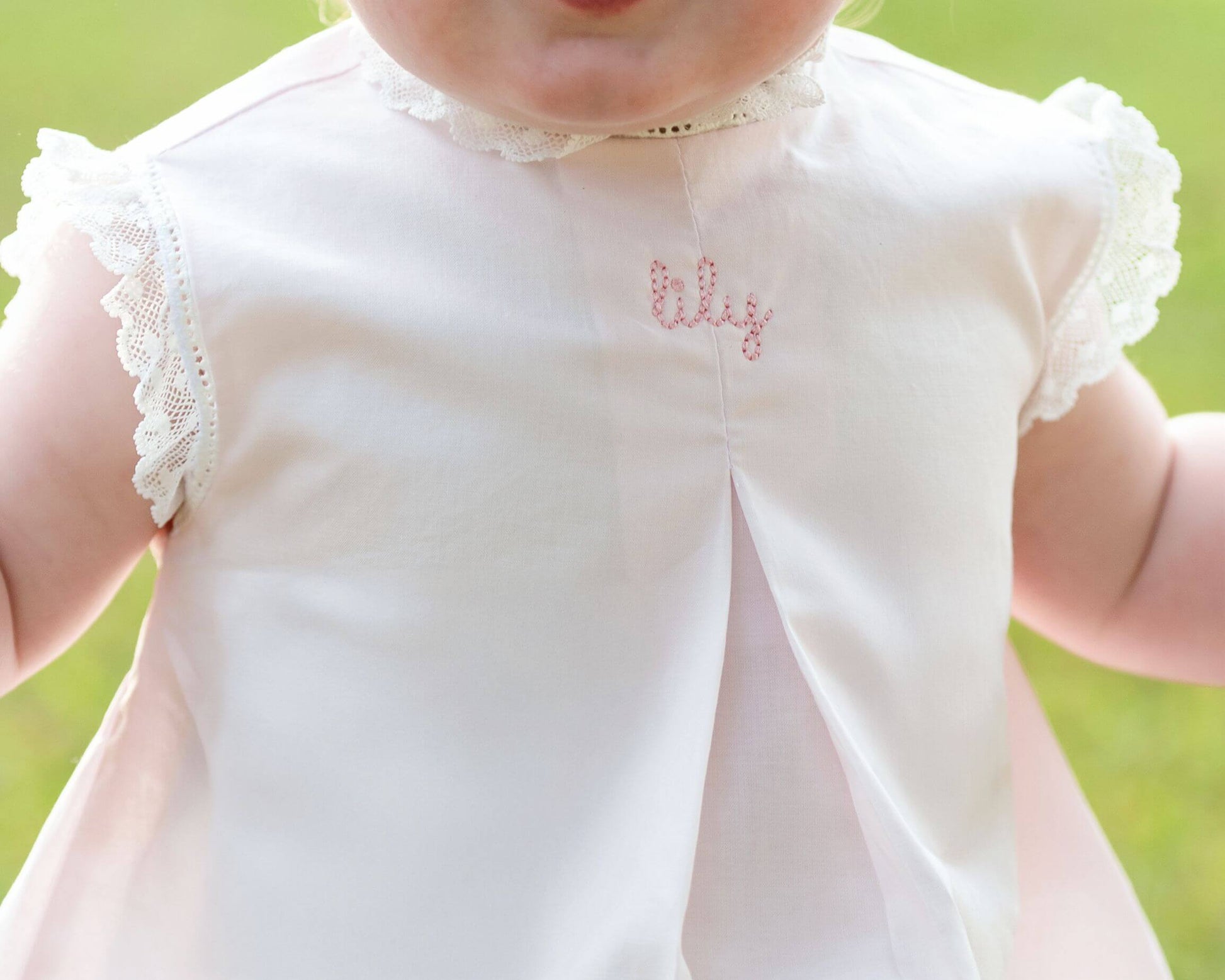 White dress with lace details and embroidered name on a blurred green background