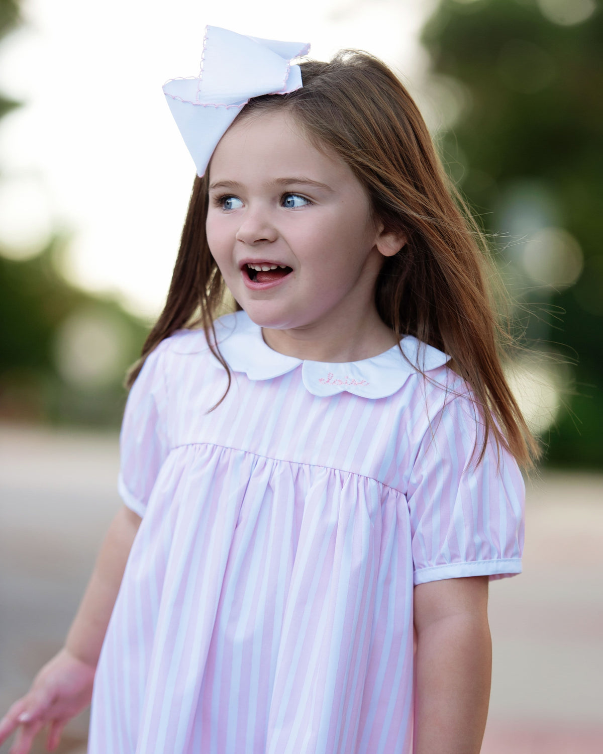 Girl wearing a pink striped dress with a white bow on her hair