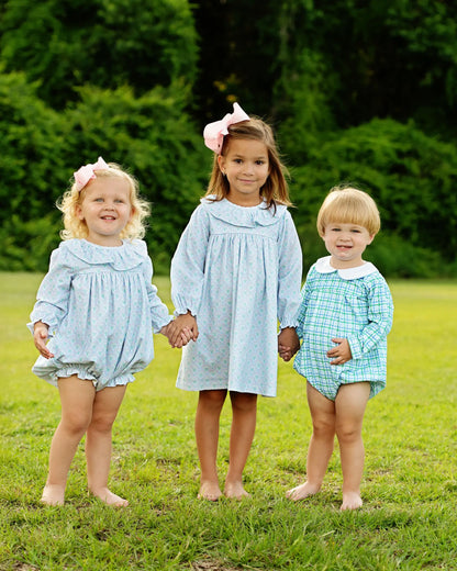 Three children holding hands in a grassy field wearing matching outfits.