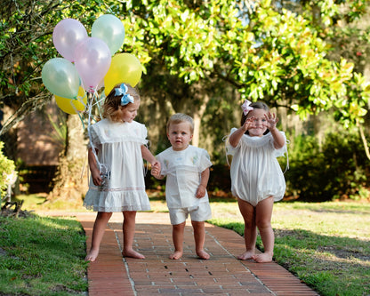 Three children walking outdoors with balloons on a brick path.
