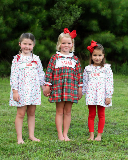 Three young girls wearing matching dresses with names printed on them, standing outdoors.