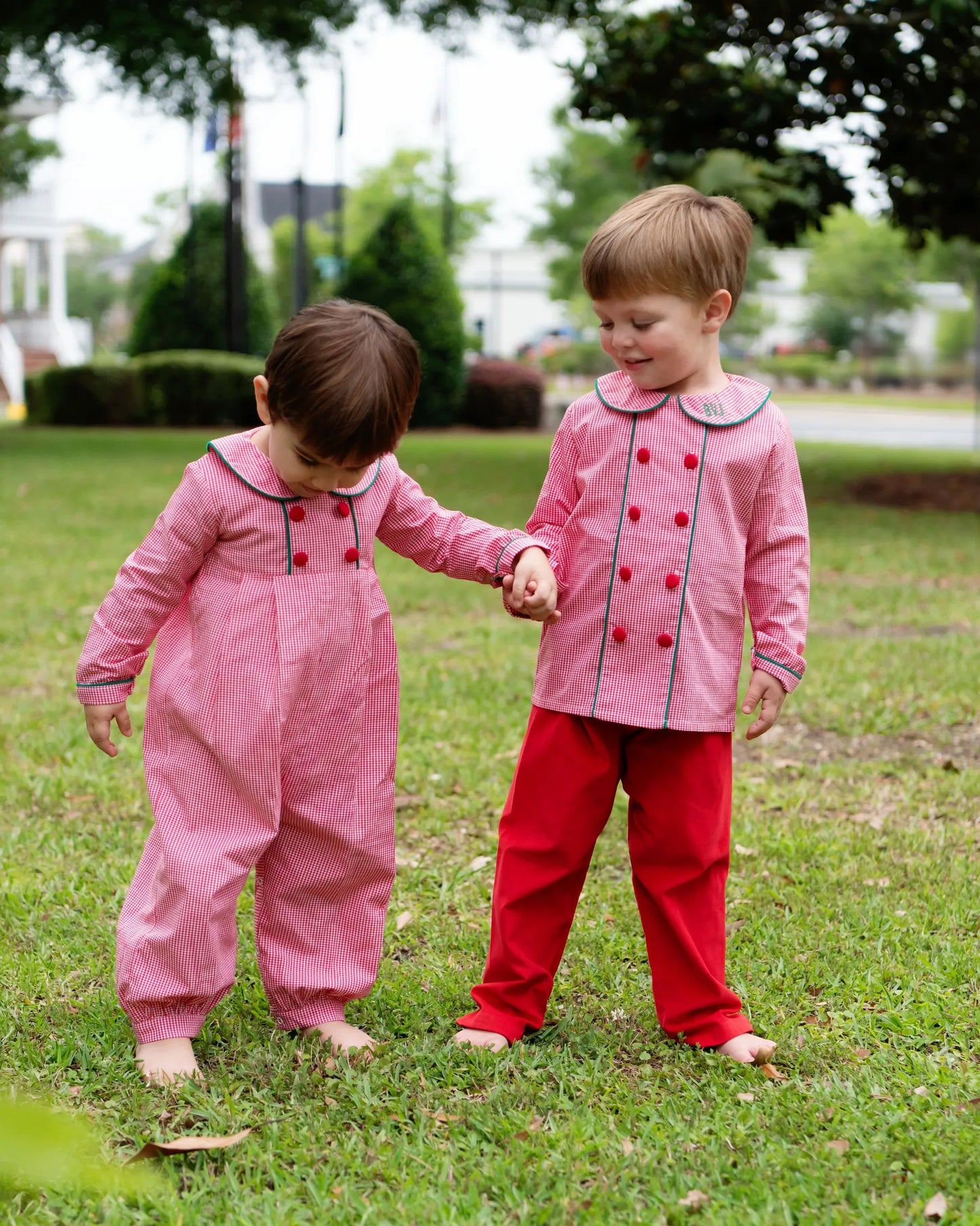 Two children in matching green and red outfits standing on grass.