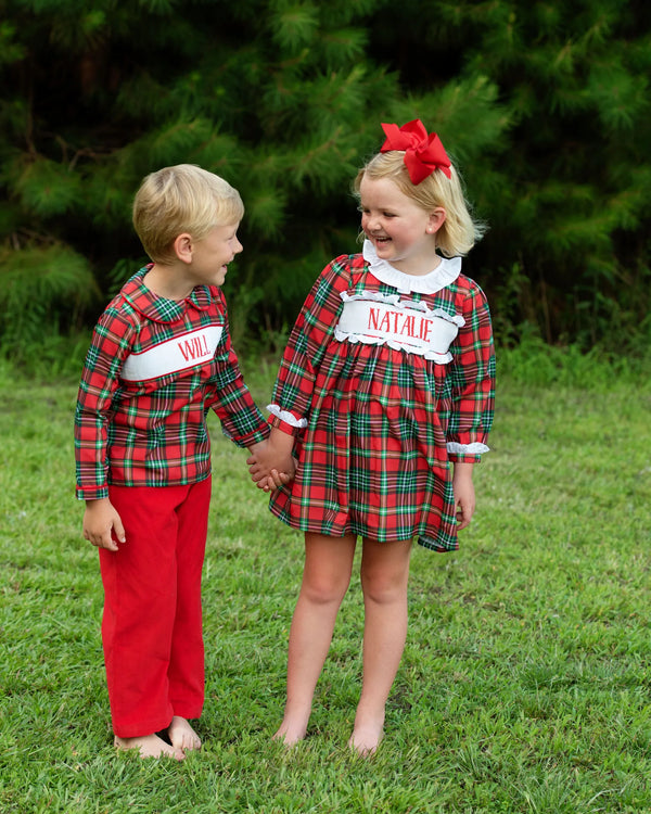 Two children in matching red and green plaid custom smocked outfits outdoors