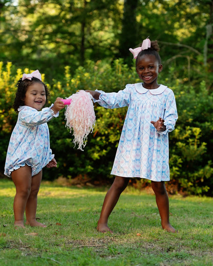Two young girls in matching dresses playing outdoors with a pink toy.