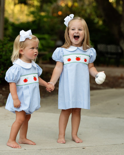 Two girls wearing matching blue gingham smocked pumpkin outfits, including the bubble