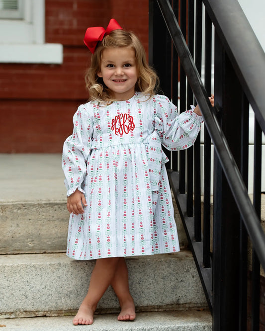 Young girl in a patterned dress with a red bow sitting on steps.