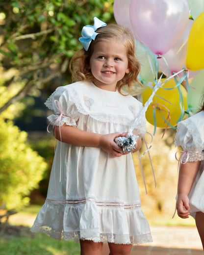 Young girl in a white dress holding balloons outdoors