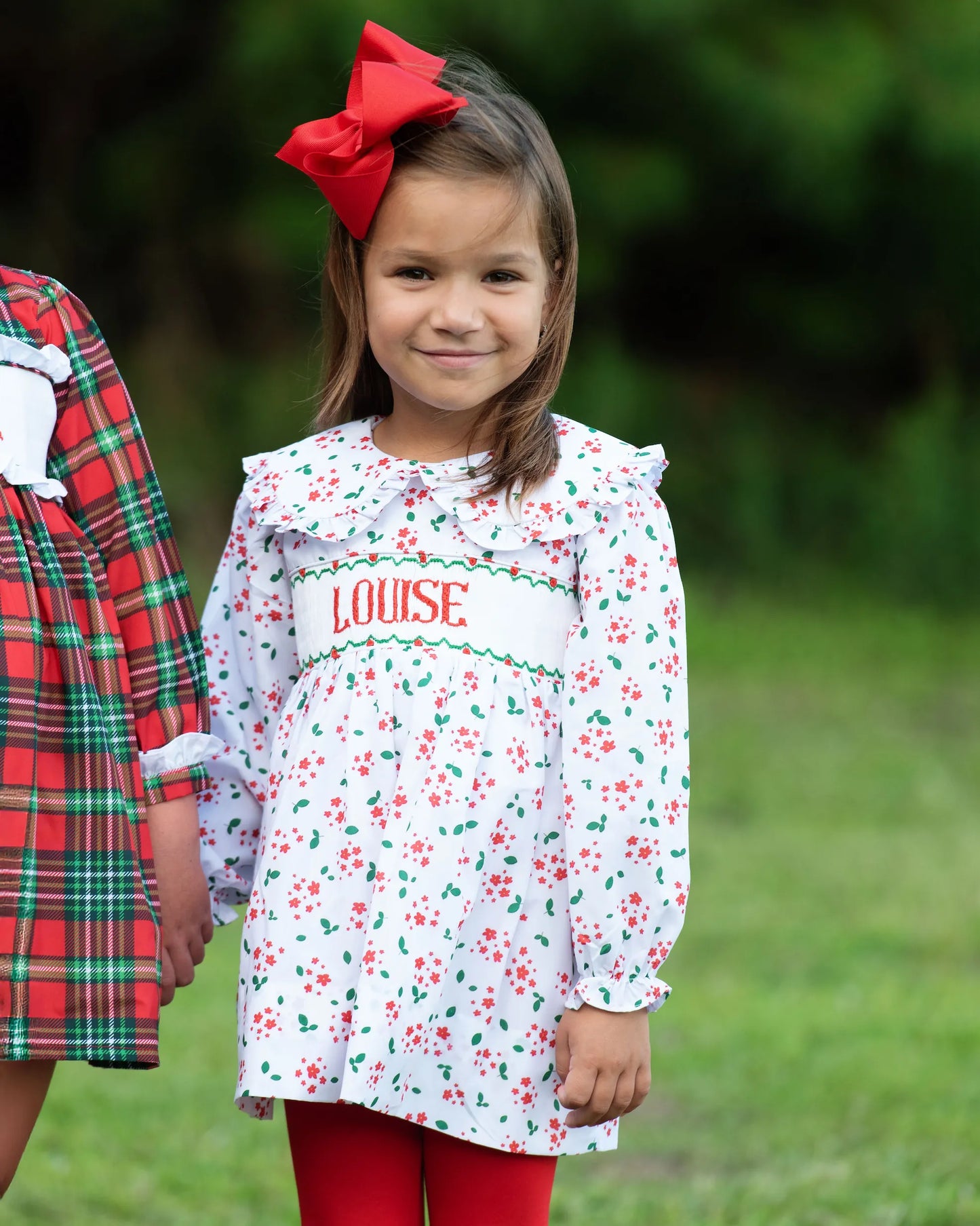 Young girl wearing a floral dress with 'LOUISE' printed on it, standing outdoors.