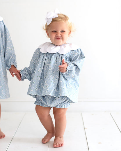young baby girl wearing a blue corduroy diaper set with small white floral print and a petal collar