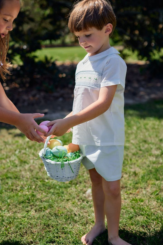 young boy holding an Easter basket, dressed in a blue and white smocked short set