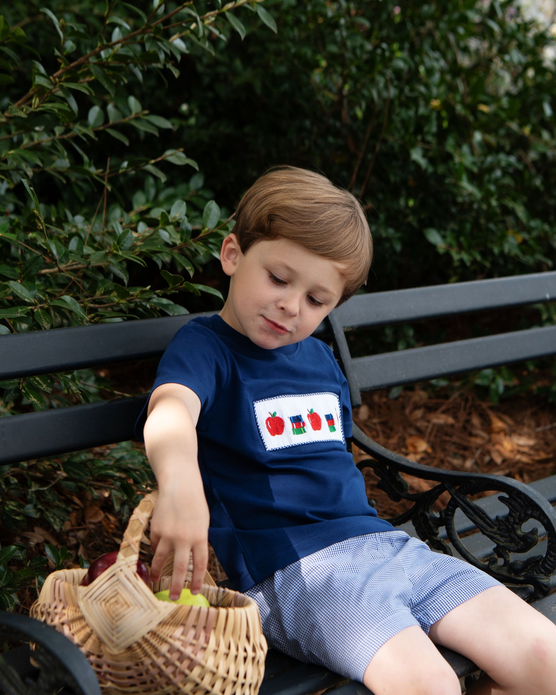 young boy wearing a back to a smocked back to school short set sitting on a bench