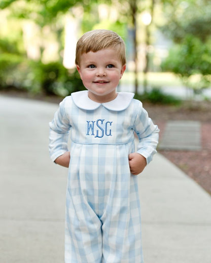young boy wearing a blue check long romper standing outside