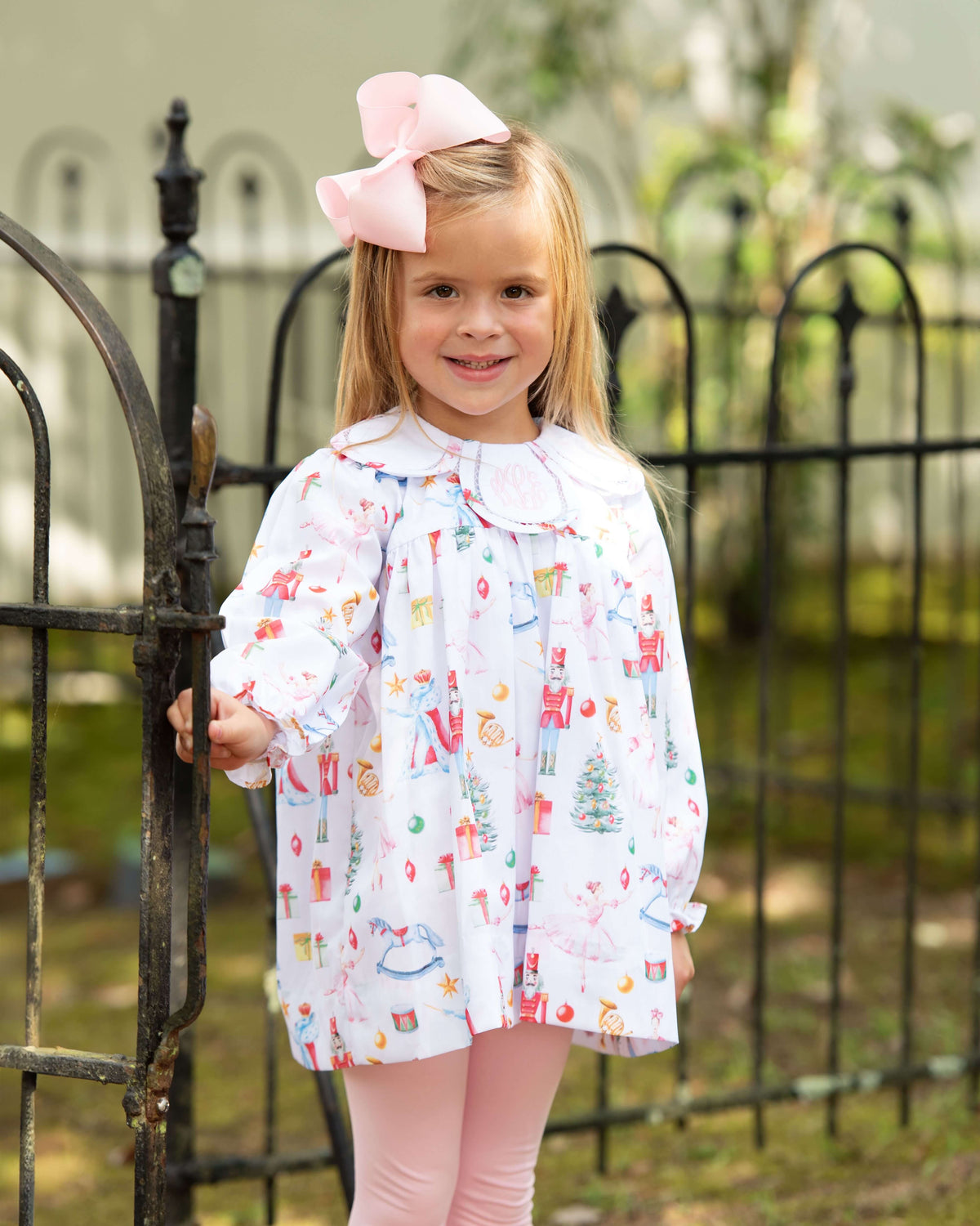 young girl standing outside by a fence wearing a nutcracker ballet legging set with a matching pink bow