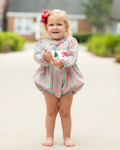 young girl standing outside wearing a red and green bubble with a smocked Christmas tree and bow