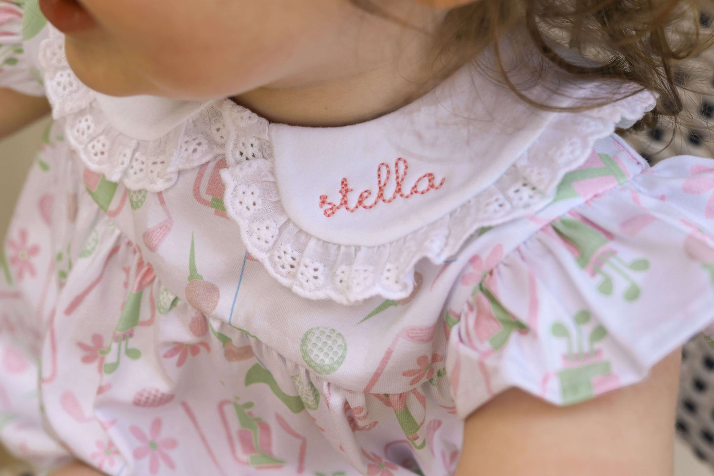 young girl wearing a golf print bubble with a monogrammed name on the eyelet collar