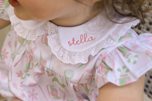 young girl wearing a golf print bubble with a monogrammed name on the eyelet collar