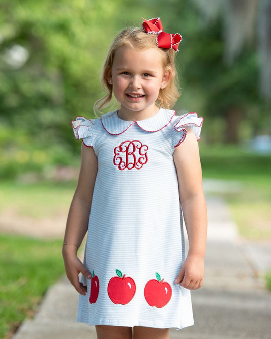 young girl wearing a knit striped dress with a trio of apples on the bottom of the dress
